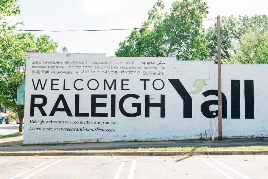 Mural on brick wall with white background and black letters reading "Welcome to Raleigh Y'all".