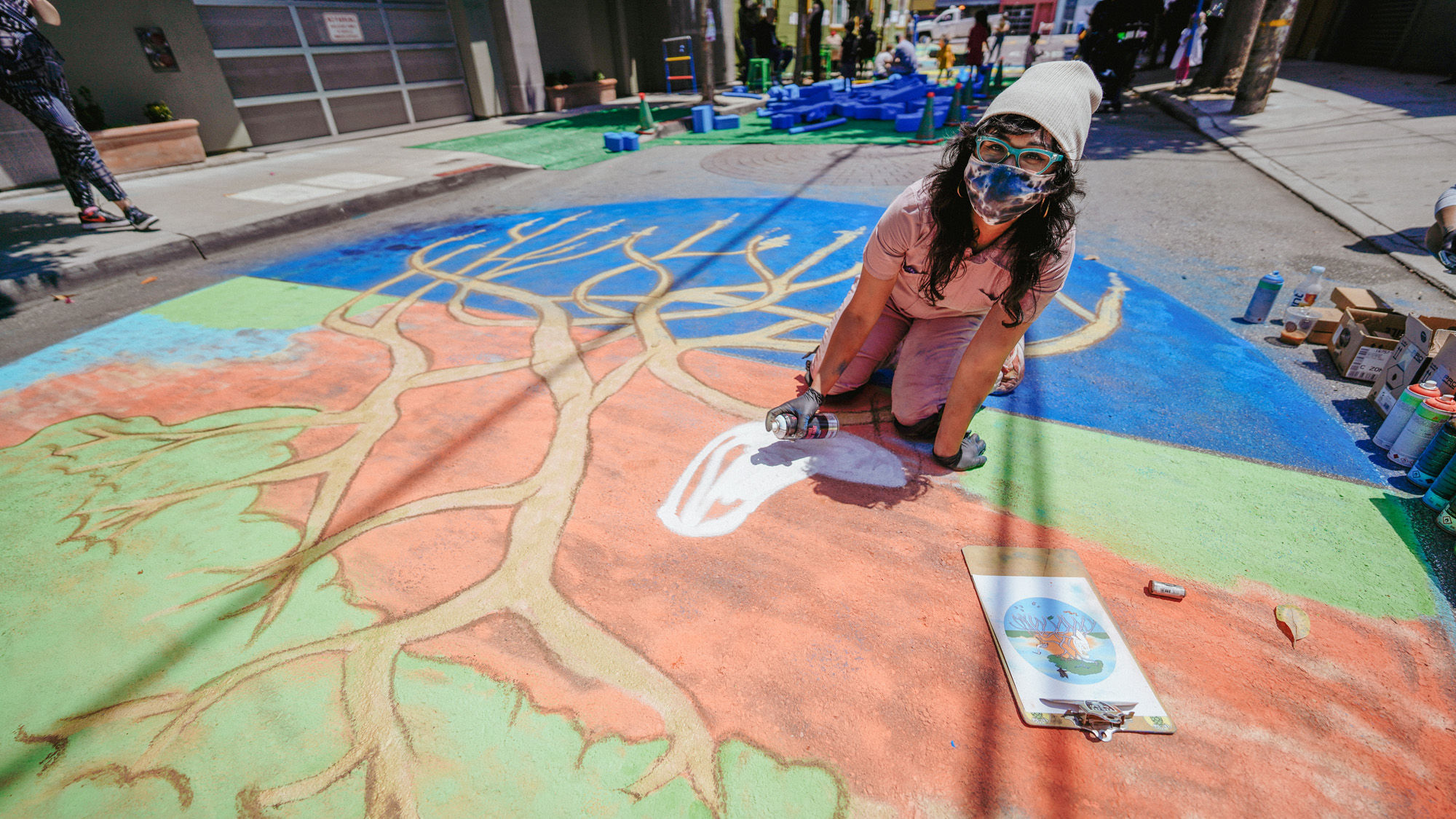 Artist Mariela Montero crouched on the pavement as she paints a large chalk mural on the ground during an event on Moss Street