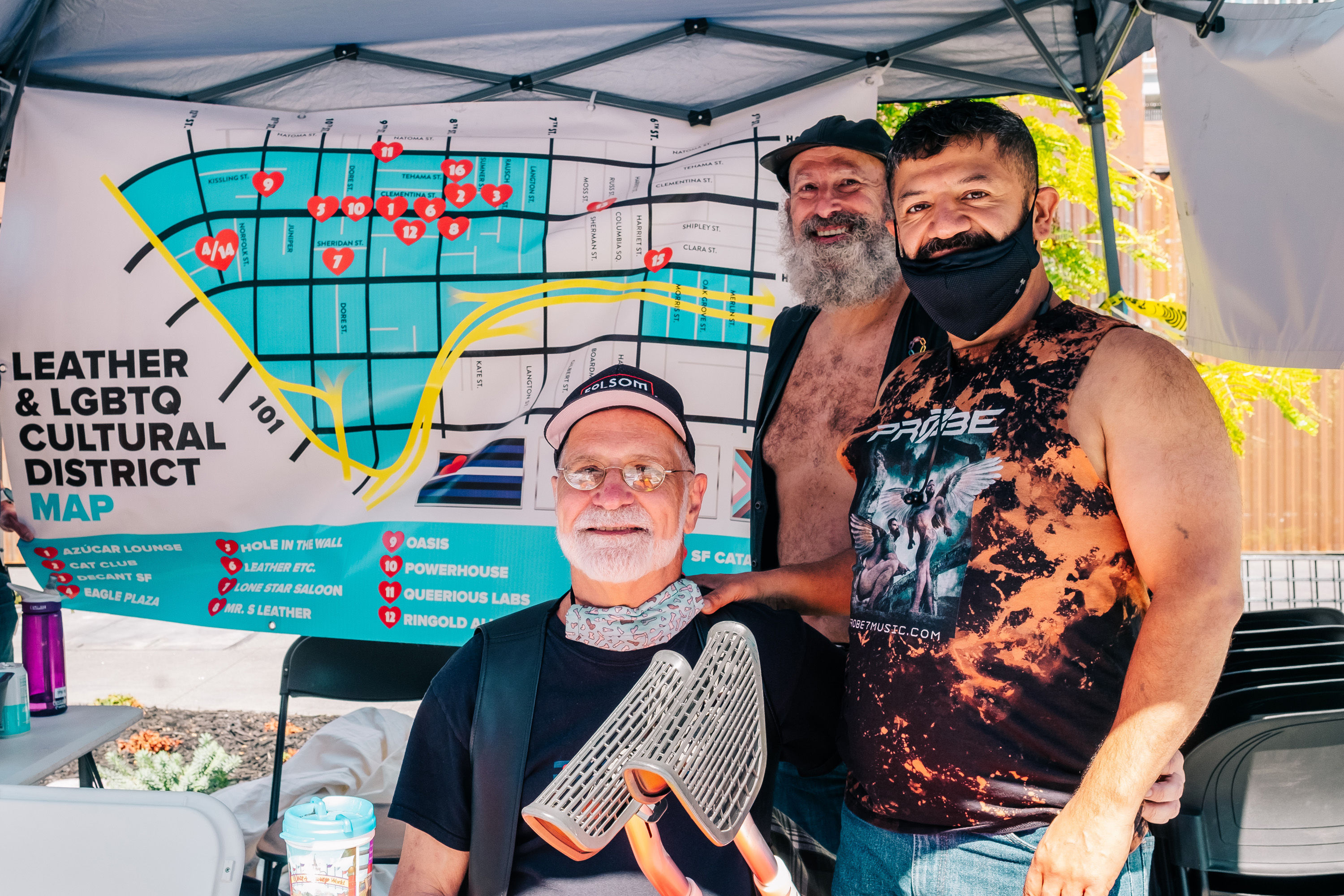 Three men from the Leather & LGBTQ Cultural District Representatives at their community booth during SOMA Second Saturdays. The Leather District map is in the background