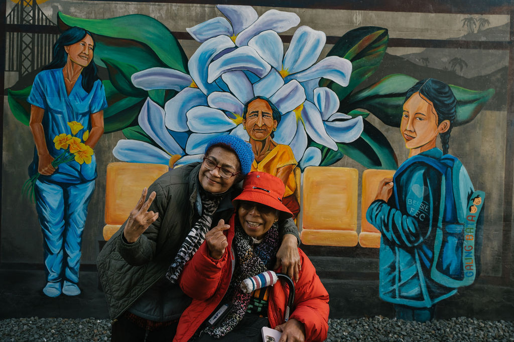 Two happy seniors from the Filipino community posing in front of the mural