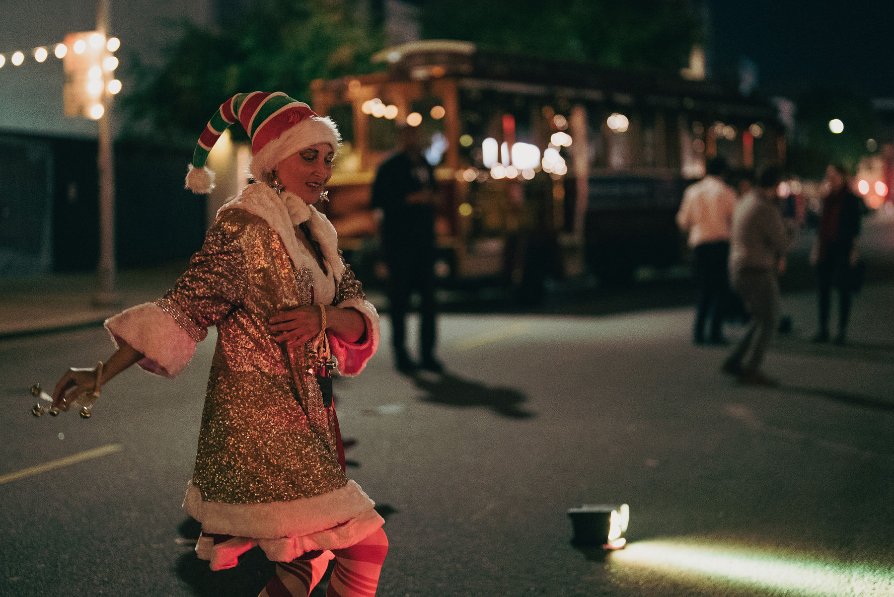 Woman dressed up as a holiday elf, dancing in front of th Holly Jolly Trolley