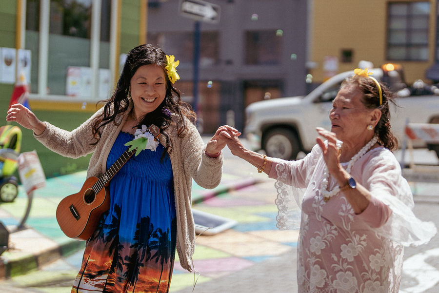 Women dancing at the Moss Street block party. The woman on the left is a ukelele player from the band Aloha Uke Squad. The woman on the right is from the Bindlestiff Seniors Restorative Theater Arts for Seniors (RETAS) program.