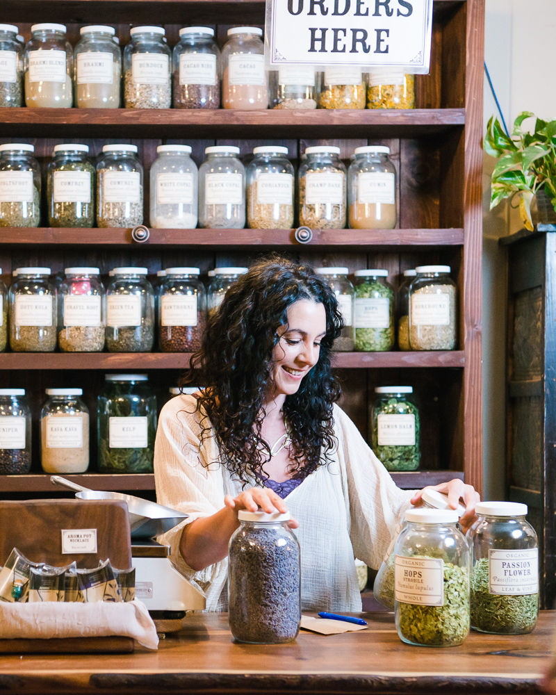 woman looks at various large jars of herbs
