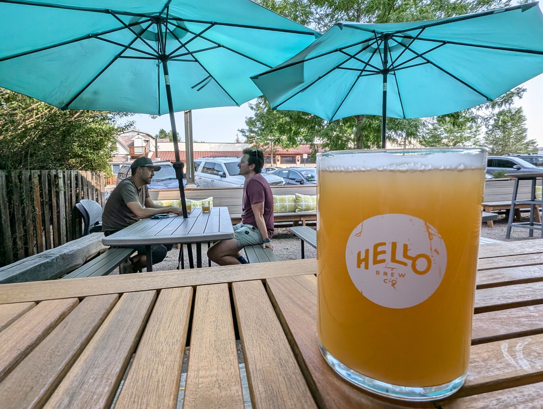 Beer and two people sitting under umbrellas on patio at Hello Brewing