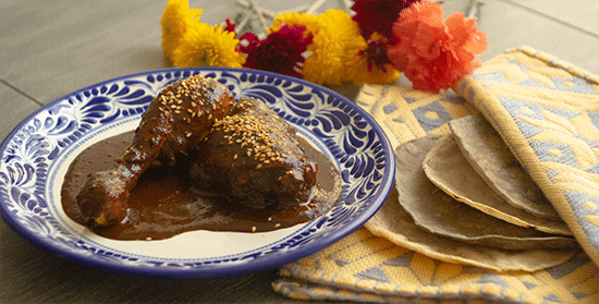 A plate of chicken covered in dark mole sauce.