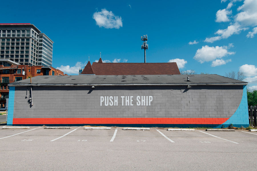 Mural on gray wall with accents of red and blue and white capitalized letters reading "Push The Ship".