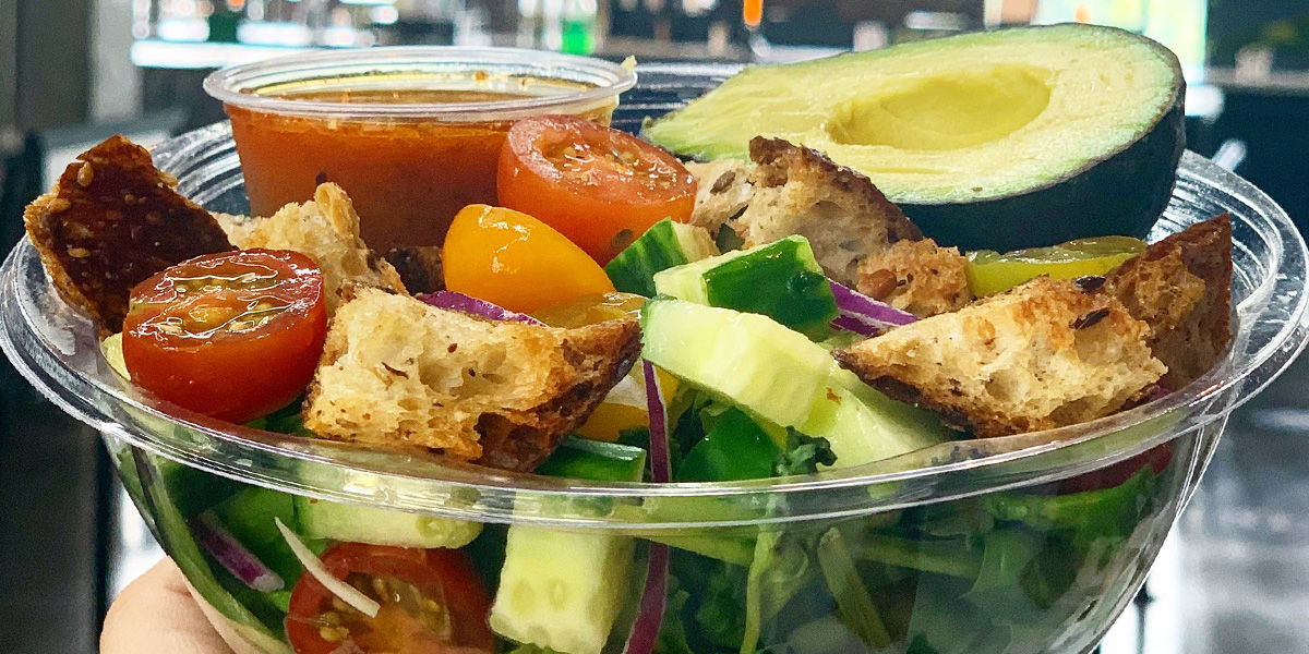 An image of a salad topped with cherry tomatoes, croutons, cucumber, and half an avocado from NOMZ at the Northside Marketplace.