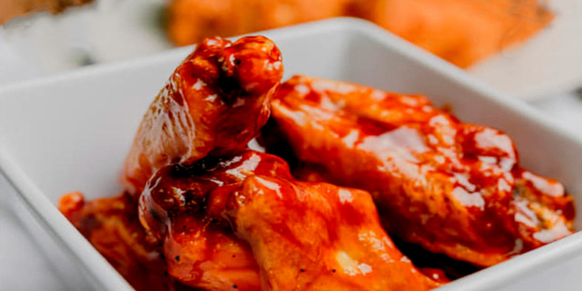 An image of chicken wings in a white, square bowl.