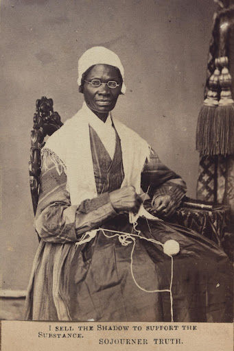A black and white photo portrait of Sojourner Truth seated in an ornate wooden chair, poised with knitting needles, and a caption that reads: 